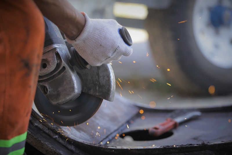 Die Hände eines Arbeiters, der mit einer Flex ein Metallrohr bearbeitet