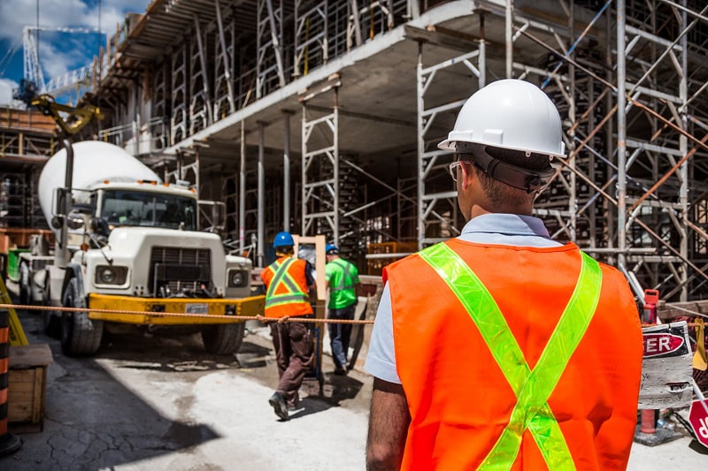 Ein Arbeiter mit Sicherheitsweste und Helm, der die Arbeiten auf einer Baustelle beobachtet